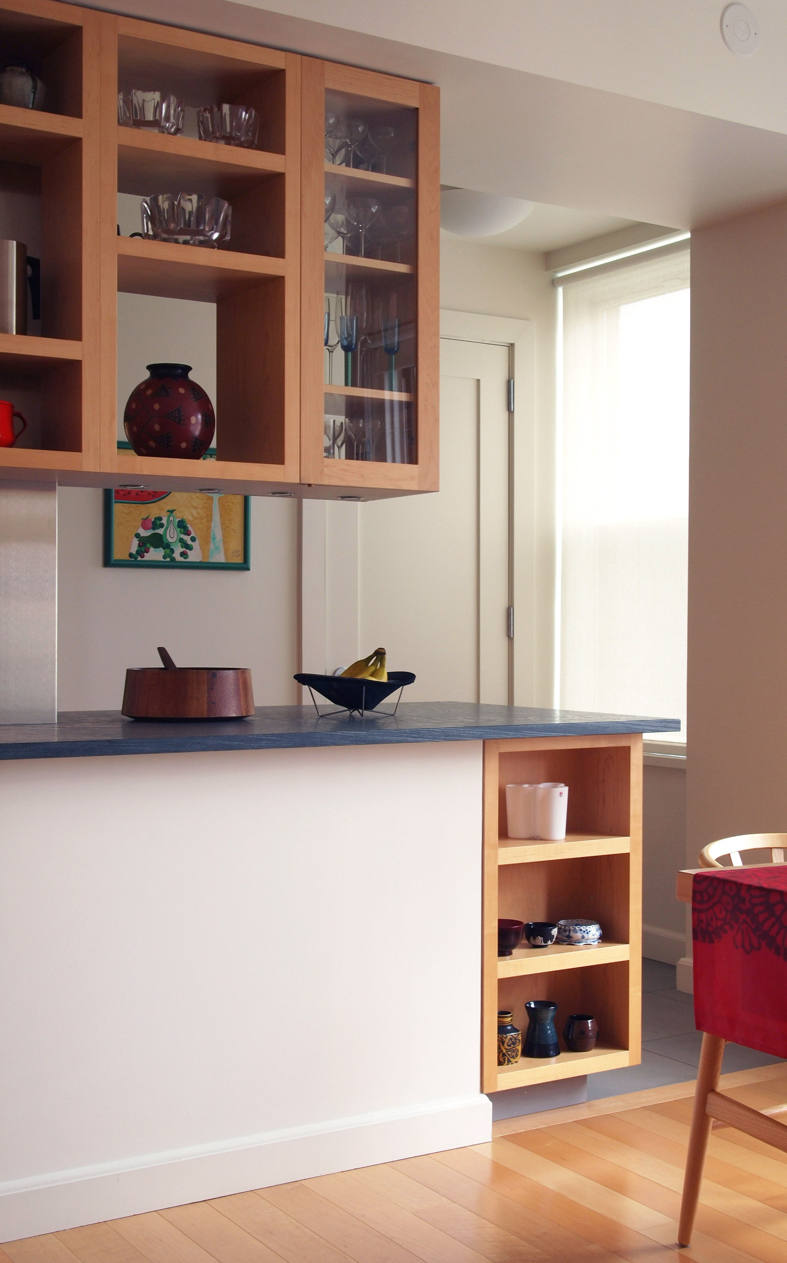 Modern kitchen with maple cabinets, open shelving, dark gray stone counters.