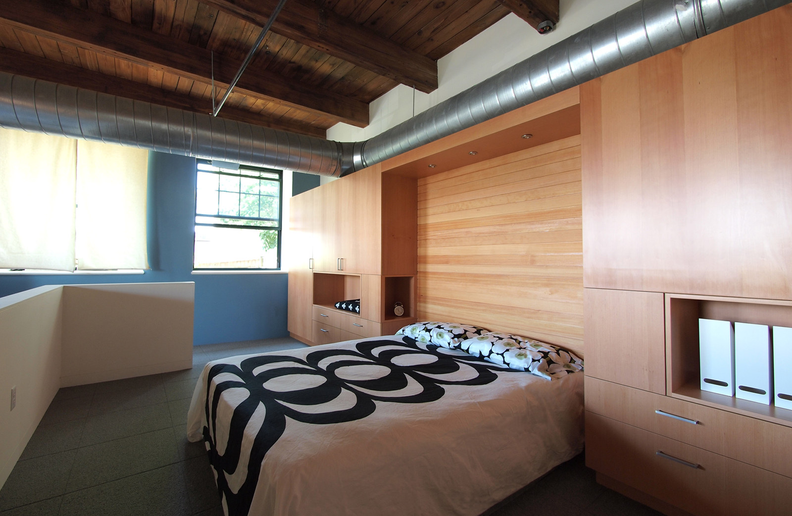 Industrial loft renovation, with modern custom built-in cabinetry around bed and custom wood headboard.