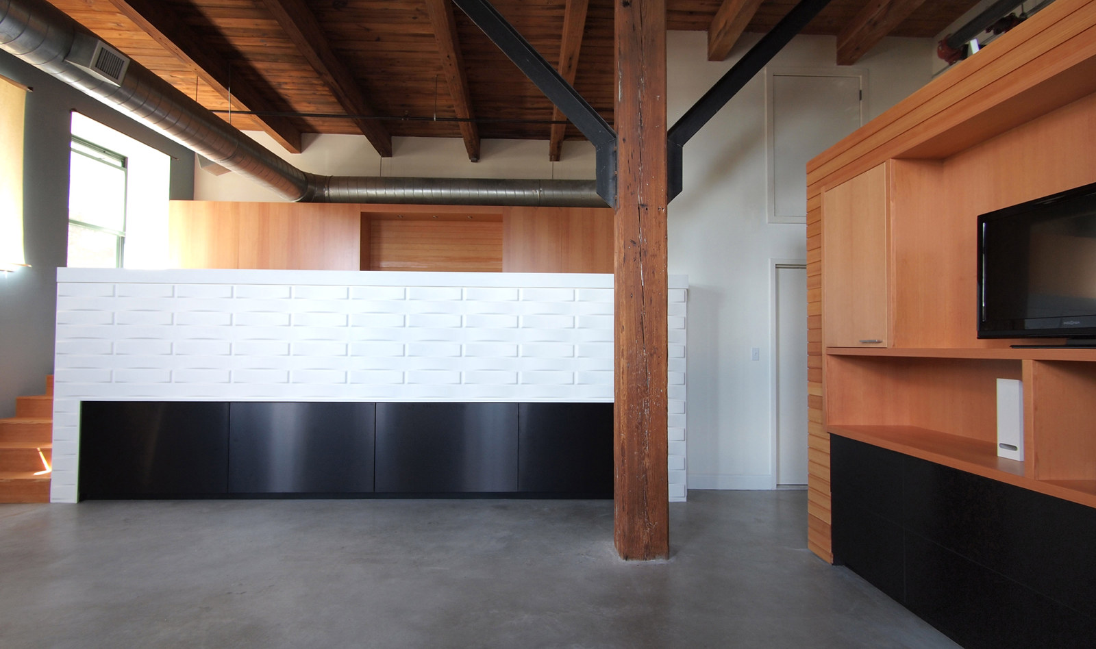 Industrial open loft renovation with exposed structure, custom cabinets, textured wall, steel-faced drawers.