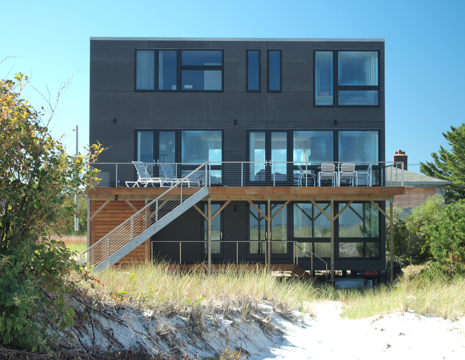 Exterior of modern house on beach in Gloucester, MA, with cement board siding and cedar deck.