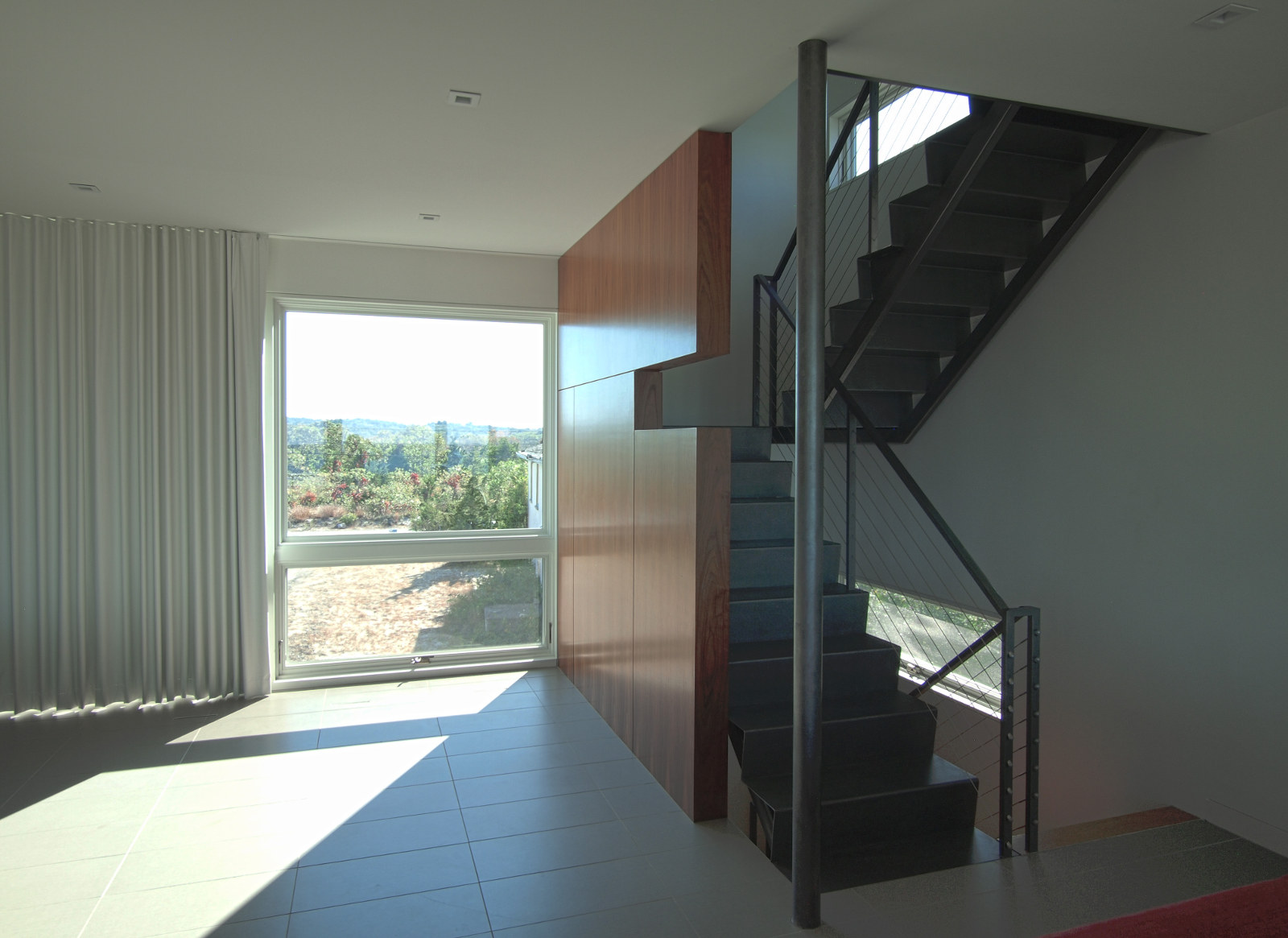 Steel stairs and stainless-steel cable railing; walnut veneer paneling at wall; large windows.
